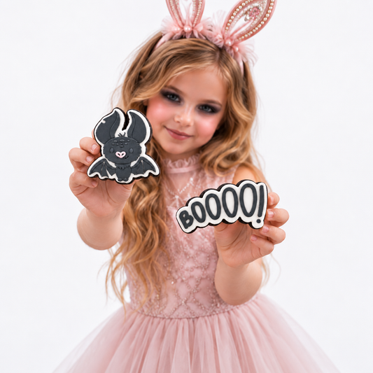 Girl wearing blush bunny ears and holding charcoal bat and BOOOO fondant sugar cookies.
