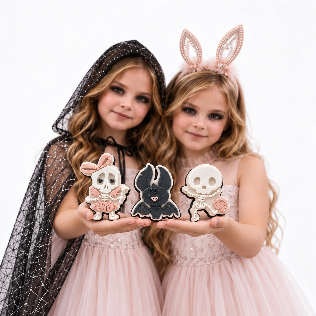 Two girls presenting skeleton and charcoal bat Halloween sugar cookies.