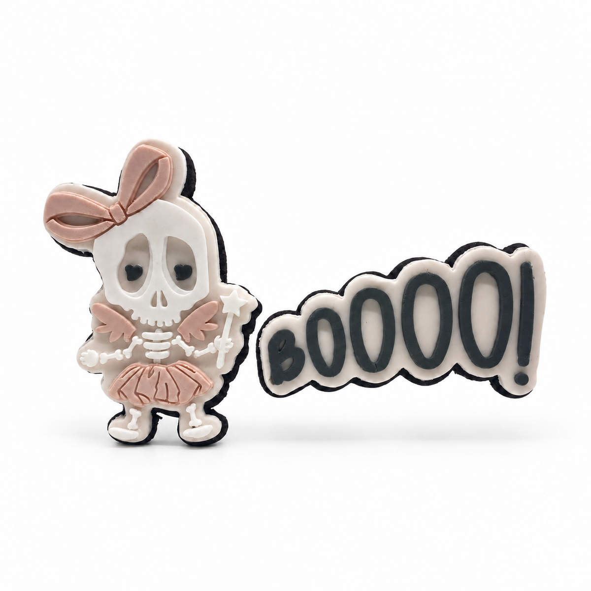 Blush skeleton fairy with a bow, wings, tutu and star wand beside a BOOOO! fondant sugar cookie on white.