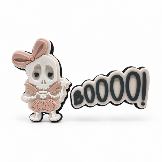 Blush skeleton fairy with a bow, wings, tutu and star wand beside a BOOOO! fondant sugar cookie on white.