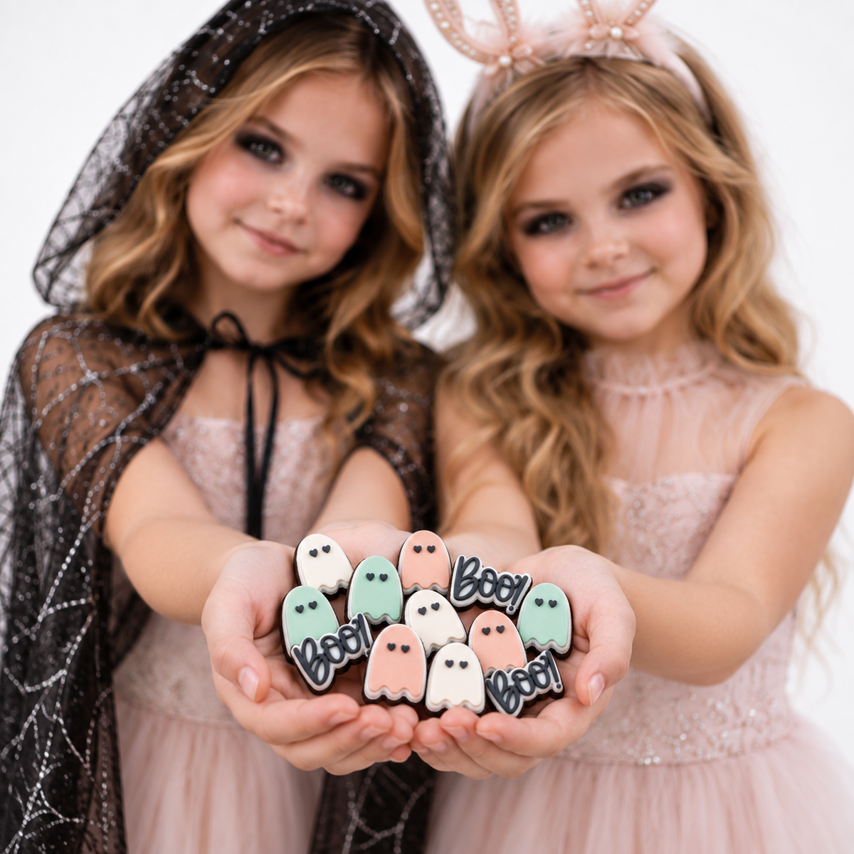 Two girls presenting pastel mini ghost and BOO fondant cookies in their hands.