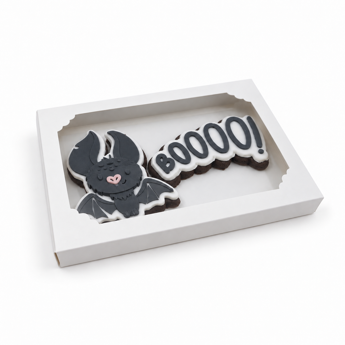 A white rectangular display box containing two Halloween-themed sugar cookies: a black bat with a small pink heart nose and wings, and a black-and-white speech-bubble cookie that says "BOOOOO!".