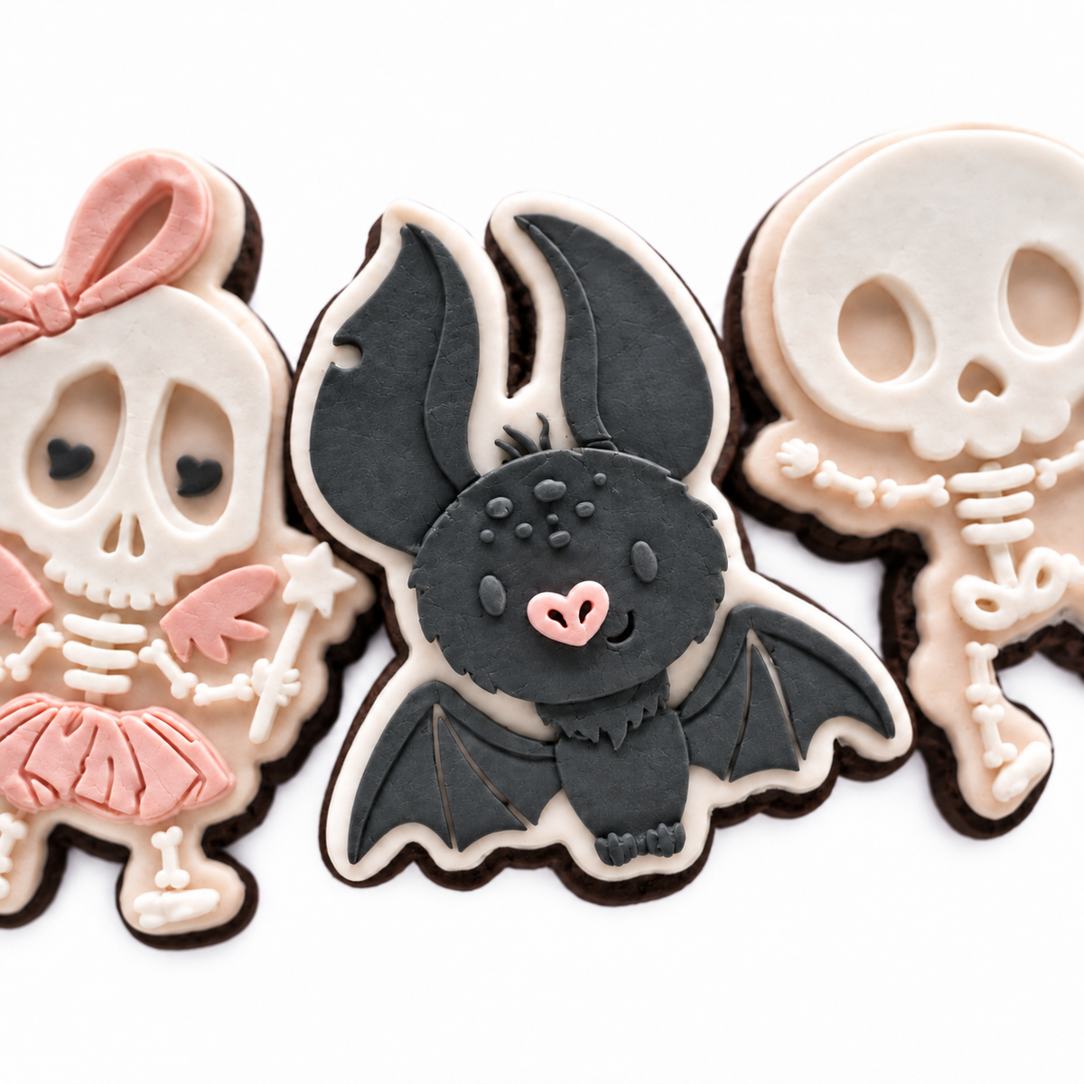 Close-up of handcrafted skeleton girl, charcoal bat and skeleton boy fondant cookies.