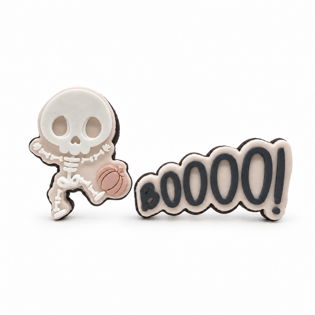 Little Bones skeleton cookie holding a blush pumpkin beside a BOOOO! fondant sugar cookie on a white background.