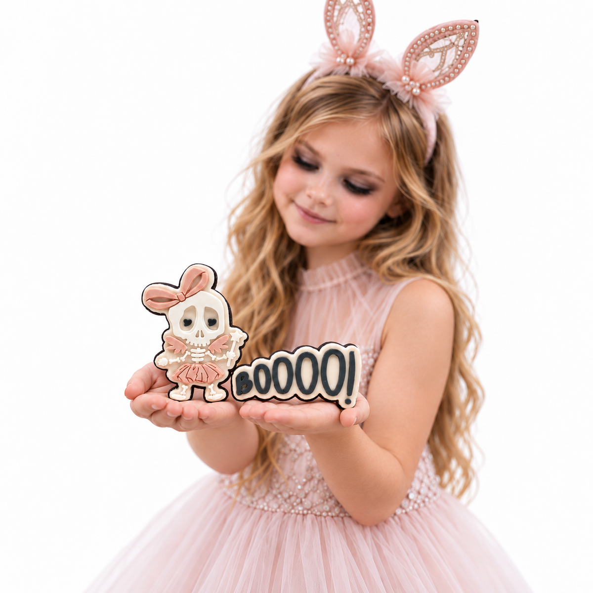 Girl in blush bunny ears looking down at skeleton ballerina and BOOOO fondant cookies.
