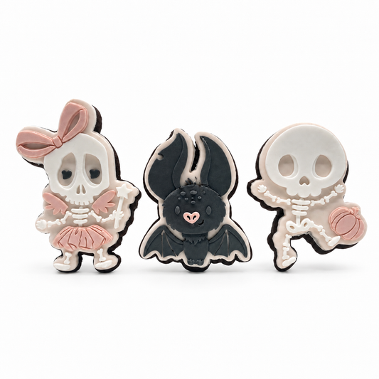 Skeleton fairy, charcoal bat and pumpkin-carrying skeleton fondant sugar cookies on a white background.